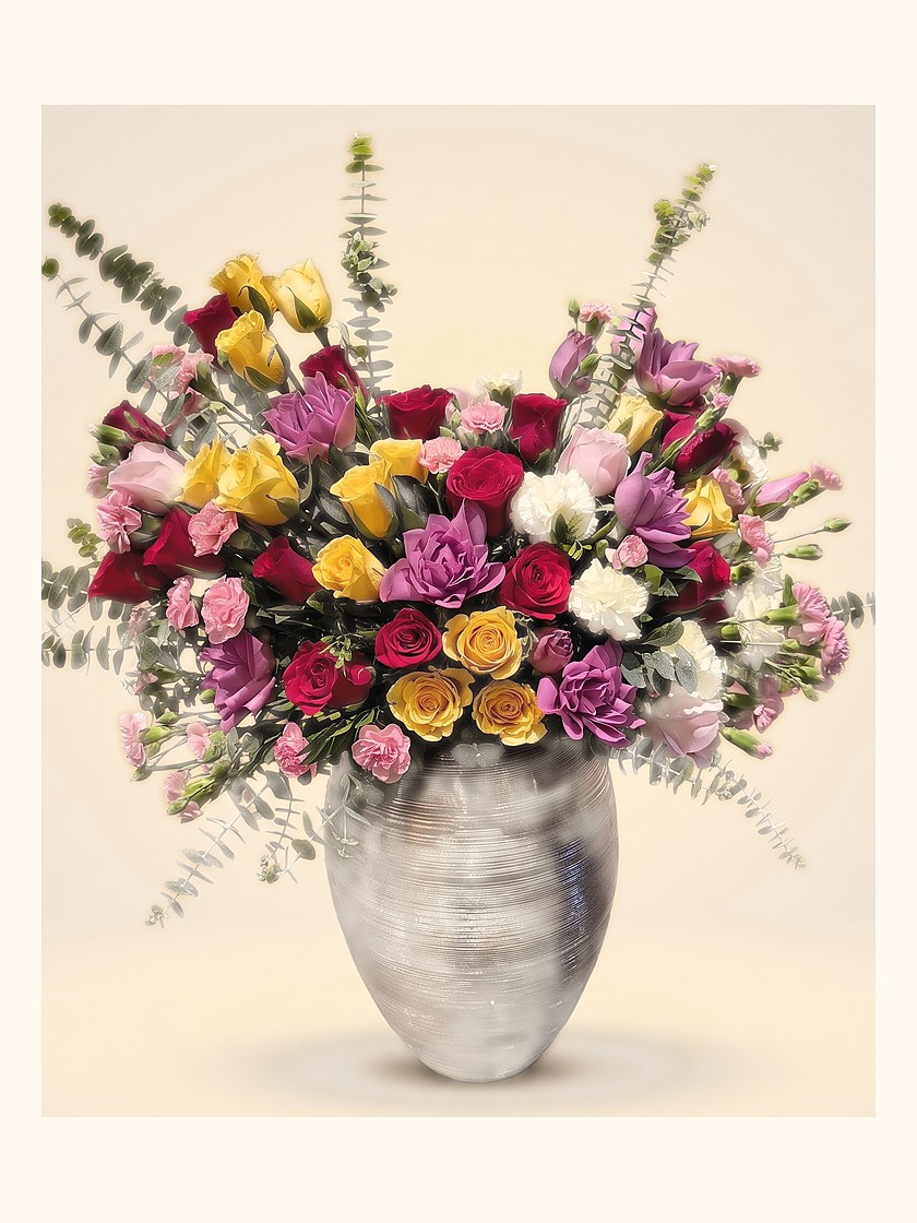 A tall arrangement of roses and eucalyptus in a brass pot