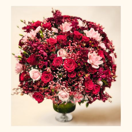 A domed arrangement of crimson and pink blooms on a footed vase